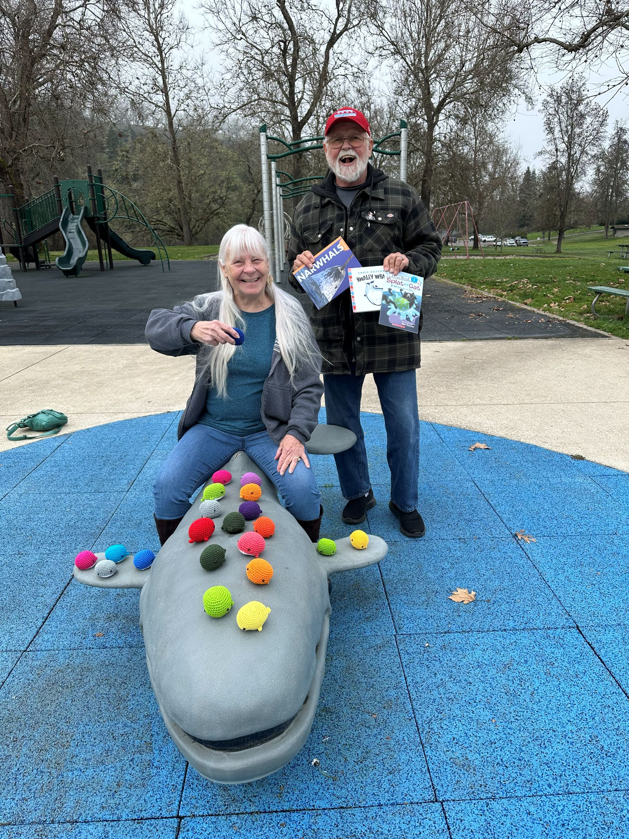 Nadine and Duke DeLaney with handmade crochet whales and sitting atop a whale structure at a playground.