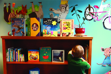 A child stands in front of a filled bookshelf with a vibrant all with children's book characters in the background