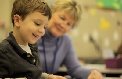 Child smiles and looks down while reading with a SMART Volunteer